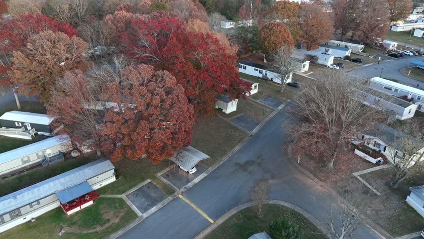 Aerial shot of an American mobile trailer home park surrounded by colorful autumn trees, quiet narrow roads and simple low-income housing area in rural suburban community. Flyover.