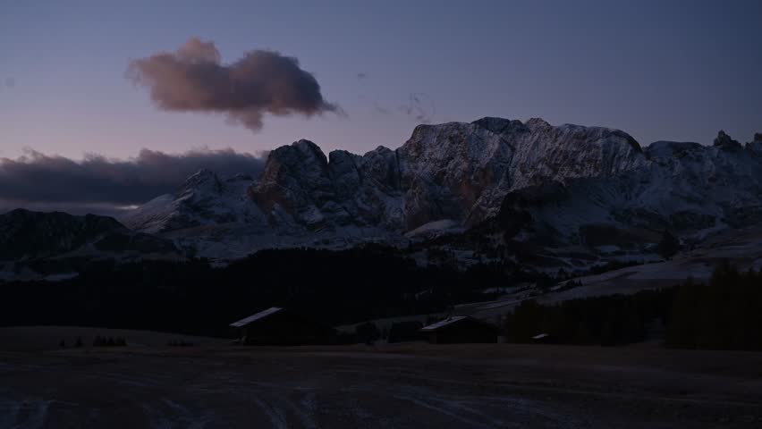 Wooden houses are on the land. Alpe di Siusi, Seiser Alm, timelapse view of majestic dolomites, mountains background
