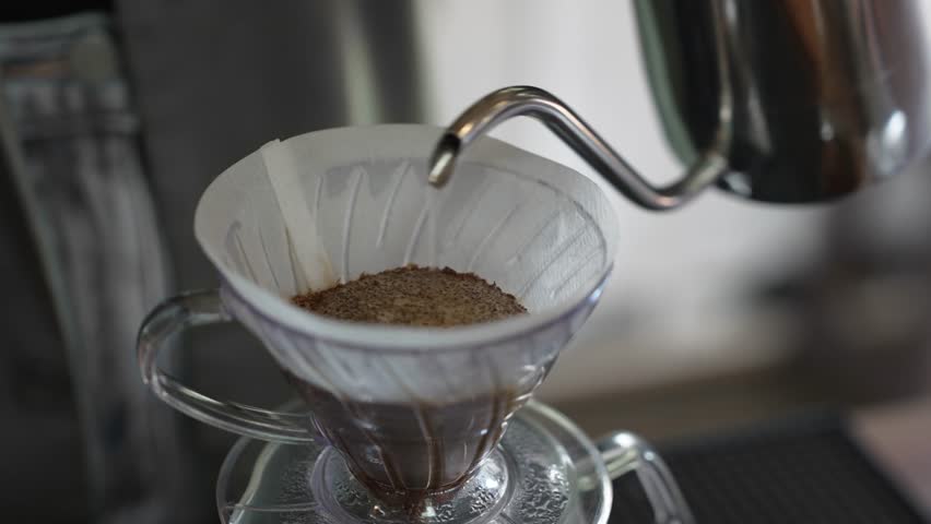 A barista prepares a pour over coffee with a controlled water pour.