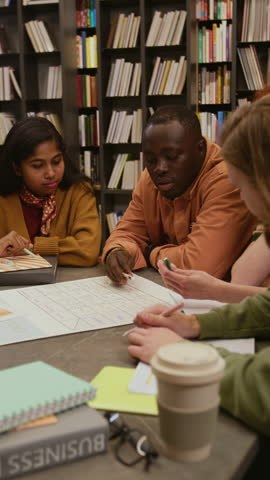 Vertical shot of African American male tutor answering students questions on English grammar rule while teaching adult learners in small study group in library