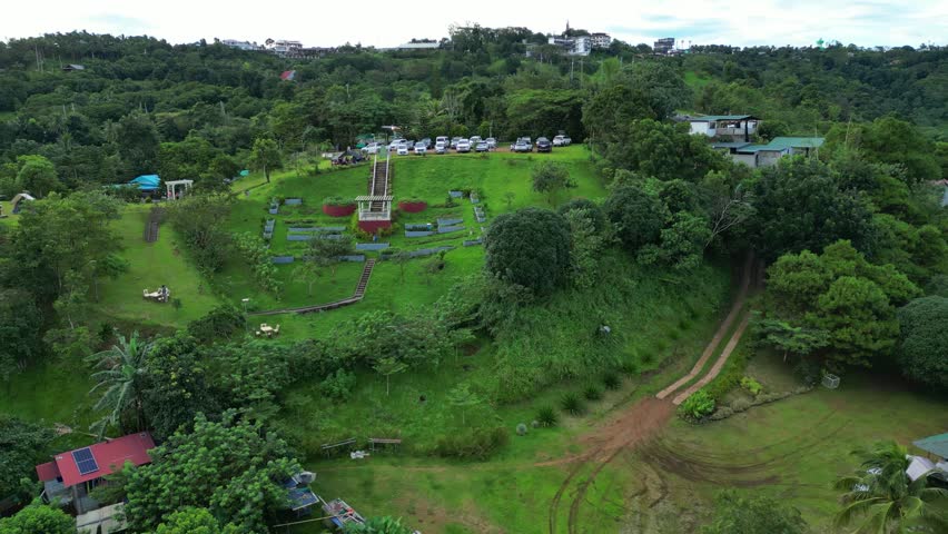 Pull-out rising aerial of Rainbow 89 Eco Park campsite with forested monument park, tropical trees, and hilly terrain in Tanay Rizal.