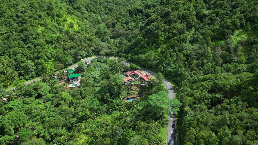 Pull-in aerial of resort hotel compound with red and green roofs, winding road, forested slopes, and hillside pool in Tanay Rizal, Philippines.