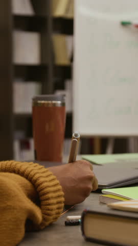 Vertical close up on hand of multiethnic young woman writing down notes during foreign language class in library