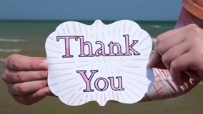 Young Woman Holds Up a Handmade Card that Says Thank You while standing at the beach in the summer at 4k Video Stock Footage - Powered by Shutterstock - Get 15% off with code: PIKWIZARD15