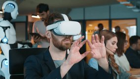 Male rotating object with hands in virtual reality headset. Coworkers focusing on computers nearby. Humanoid robot interacting with male holding tablet in background. Digital workflow. - Powered by Shutterstock - Get 15% off with code: PIKWIZARD15