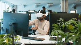Male operating system inside virtual reality world while wearing VR headset. Moving arms to interact with digital interface. Office environment with coworkers working at computers nearby. Active tasks - Powered by Shutterstock - Get 15% off with code: PIKWIZARD15