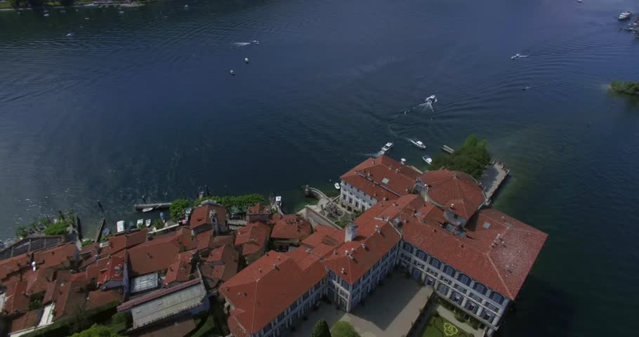 Expansive drone shot of the historic Isola Bella island on Lake Maggiore, Italy, featuring the Palazzo Borromeo and the dramatic baroque tiered gardens. The view captures the entire complex with a sma