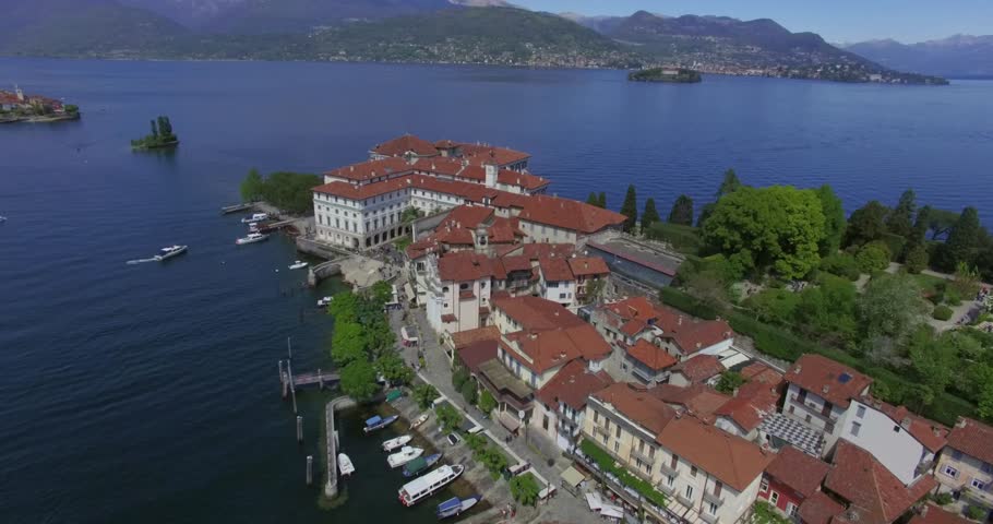Expansive drone shot of the entire Isola Bella island on Lake Maggiore, Italy, highlighting the Palazzo Borromeo with its red tile roof, the surrounding historic village and marina