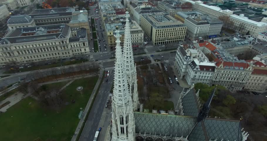 High-angle aerial view of a grand European city  Vienna featuring the prominent twin Gothic spires of a historic church Votivkirche towering over dense surrounding classical architecture and city stre