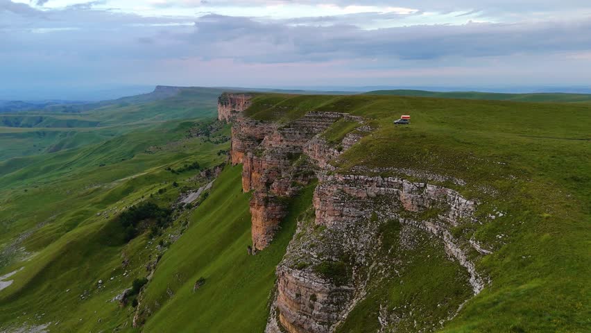 a motorhome is parked on the edge of a cliff overlooking the Gumbashi Pass in the Caucasus during a colorful sunset