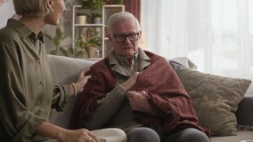Medium shot of adult Caucasian woman checking fever of senior father with flu sitting on sofa at home - Powered by Shutterstock - Get 15% off with code: PIKWIZARD15