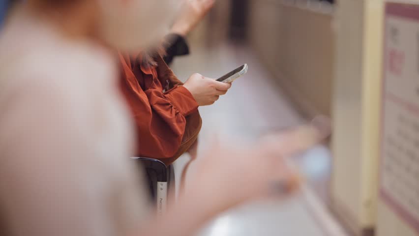 Slow motion close-up of a woman using her smartphone while waiting on a platform at a Japanese metro station. She stands calmly, waiting for her destination.