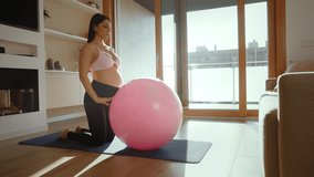 Beautiful pregnant woman practicing pilates exercises with a fitness ball in her living room, promoting health and well-being during pregnancy - Powered by Shutterstock - Get 15% off with code: PIKWIZARD15