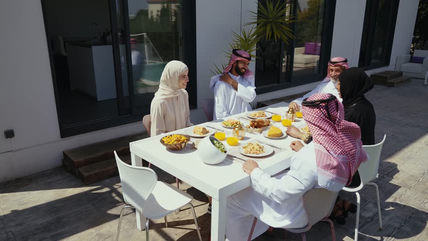 Muslim family celebrating eid al-fitr outdoors, sharing traditional dishes at a modern backyard dining table beside a swimming pool, multi-generational joy and togetherness