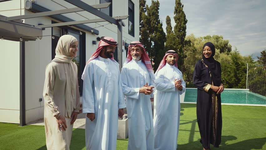 Arab family across generations in traditional dress—thobes, keffiyehs, hijabs and abaya—chatting and smiling outdoors by a modern house, garden patio atmosphere of warmth and togetherness