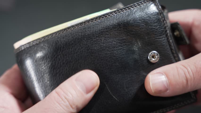 Close-up of hands opening a wallet packed with euro banknotes, showing cash savings. Shallow depth of field highlights the thick stack of bills.
