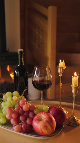 Slow living scene with wine, fruits and candles by fireplace. Cozy interior