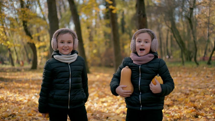 Two twin sisters dance and play while listening to music in the park. A few happy children are playing briskly, throwing leaves in the air, while others sit nearby, enjoying the rhythmic music coming from their phones.