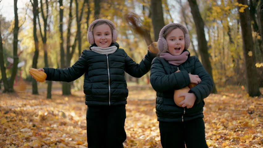 Two twin sisters dance and play while listening to music in the park. A few happy children are playing briskly, throwing leaves in the air, while others sit nearby, enjoying the rhythmic music coming from their phones.