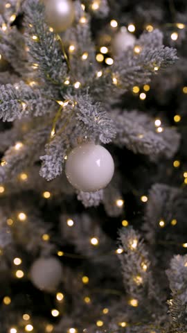 A hand gently hangs a white ornament on a snowy Christmas tree decorated with warm fairy lights