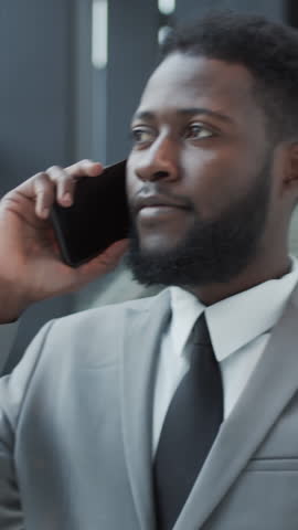 Vertical shot of bearded African American man in suit smiling while having important business phone call