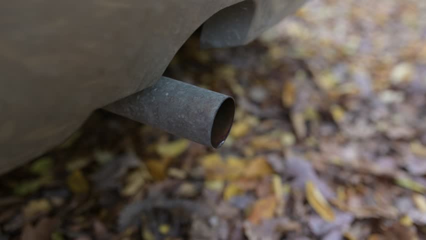Close-up of a car exhaust pipe shaking as the engine revs, emitting bursts of condensation and sound while the vehicle accelerates. Video with sound
