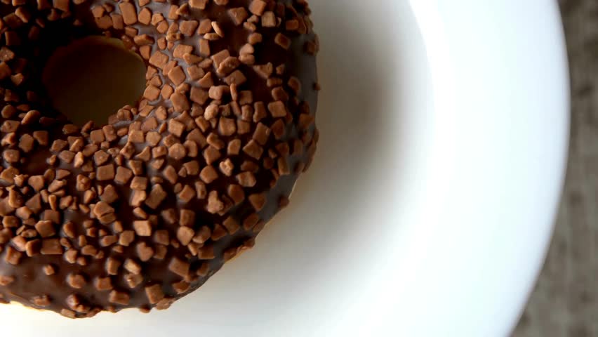 Round chocolate donut with a glossy glaze and crunchy sprinkles displayed on a clean white plate. Ideal for sweet treat and bakery content.