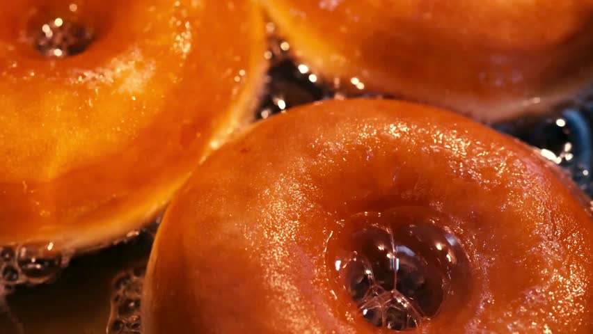 Hot oil bubbles around several donuts as they fry. Donut becomes golden brown with sweet smell. Delicious snack, tempting bakery treat being made in kitchen.