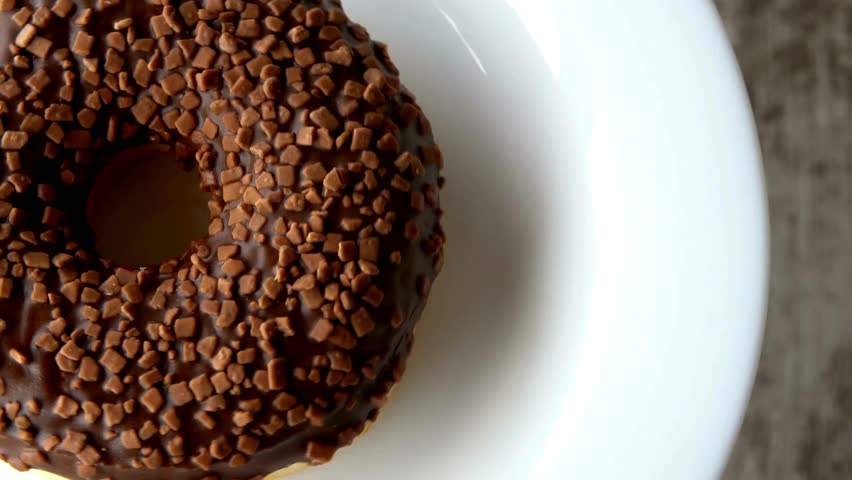 Decadent chocolate donut covered in rich frosting and sprinkled with crunchy toppings sits on a white plate. Perfect sweet treat for food lovers.