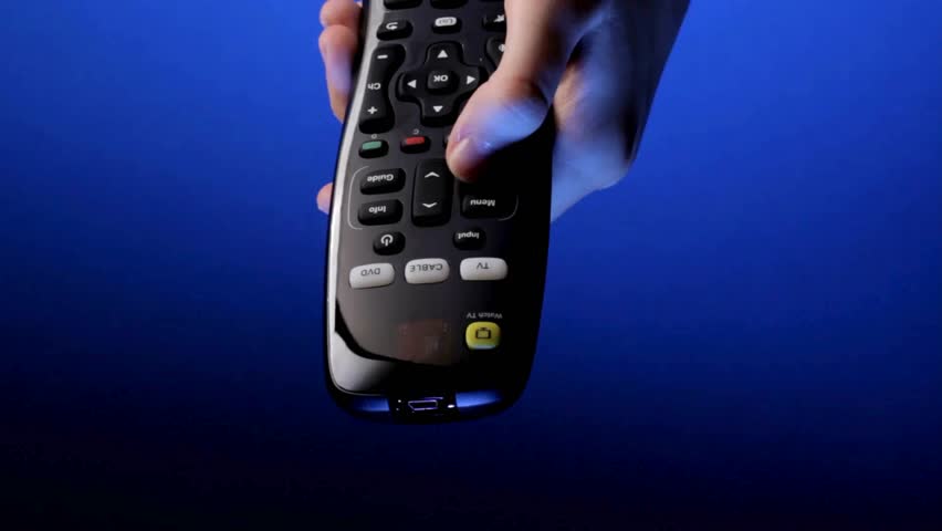 A Person Sitting on sofa while flipping through TV channels with remote control in hand. A hand controlling TV and movie channels. Close up shot of a remote control in a man's hand.