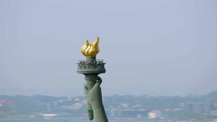 View of Liberty's torch reaching towards the sky, symbolizing freedom and hope. City buildings form a blurred backdrop, enveloped in early morning haze. This moment captures calming ambiance.