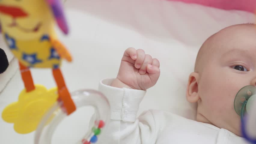 Newborn is awake in crib with hanging toys over him. 1 month old baby looking at hanging baby mobile with selective focus. Handheld high angle shoot with shallow depth of field