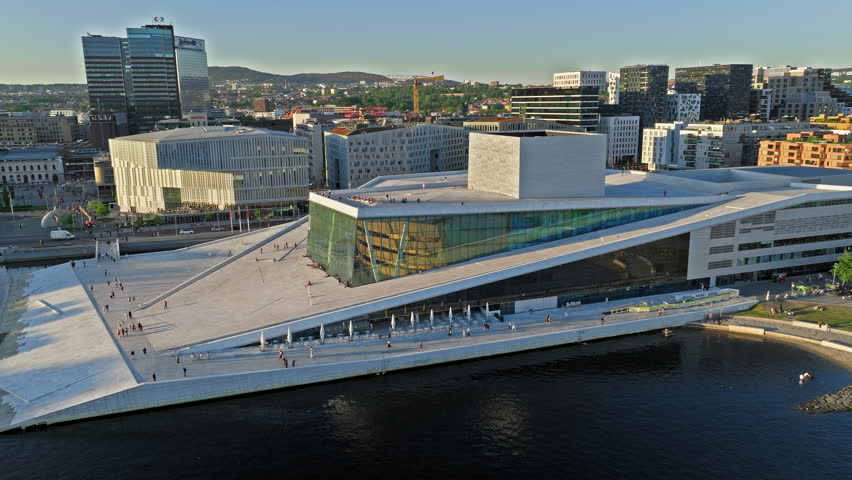 Aerial orbit over Oslo Opera House waterfront zone. Clean summer daylight tourism drone view showcasing fjord panorama, pedestrians and modern Nordic city vibe.