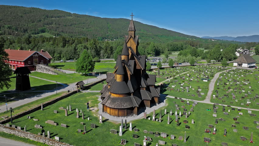 Wide drone pullback of the wooden Heddal Stave Church and surrounding cemetery in Notodden Norway. Sunny summer morning tourism shot capturing rural Scandinavia travel lifestyle.