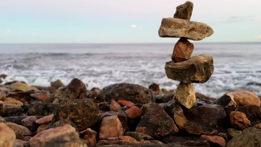 Atmospheric zen stone balance beside the ocean at sunset, gentle waves and serene warm light. Ideal for meditation, wellness, mindfulness, relaxation content and nature-themed projects. Unique seascape #10.