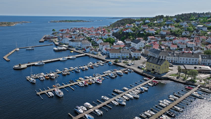 Aerial view of Risor Norway harbor with boats and colorful wooden houses along the waterfront. Sunny summer coastal town scene with islands and bright blue sea.