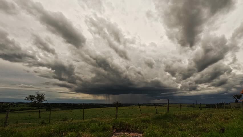 A storm over a farm field, seen in the distance, approaches rapidly with extremely heavy clouds on a late afternoon in Brazil.