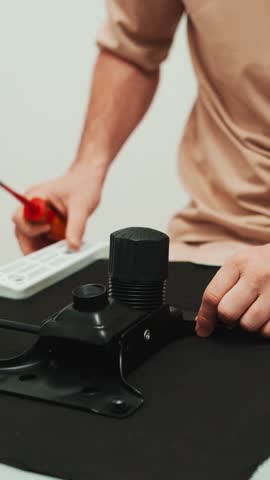 Worker adjusts white office chair tightening screw with tool, focusing on repair accuracy, stable construction. Closeup shot shows manual setup supporting ergonomic comfort in modern home workspace.