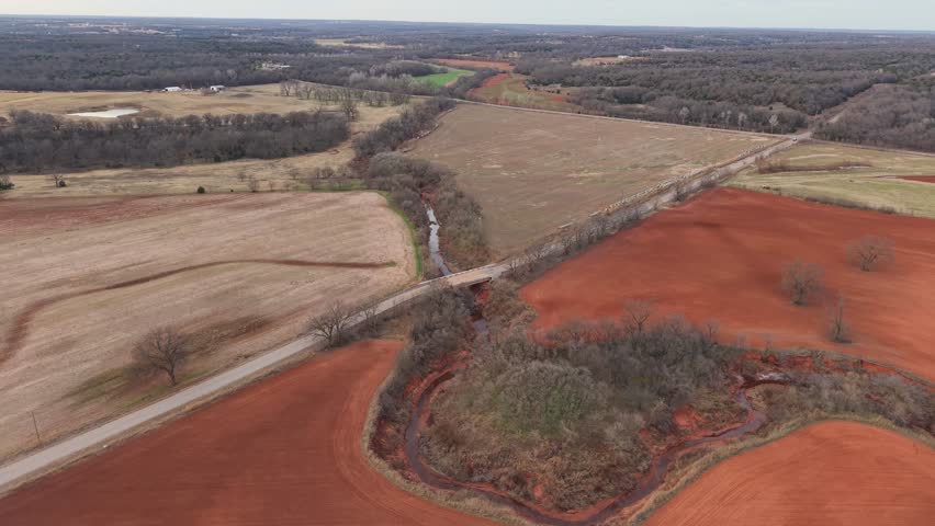 Cinematic orbit over red dirt Oklahoma creek - seasonal series (winter 2) Aerial drone shot of central Oklahoma farmland with red soil fields and a winding river. Crisp winter colors.