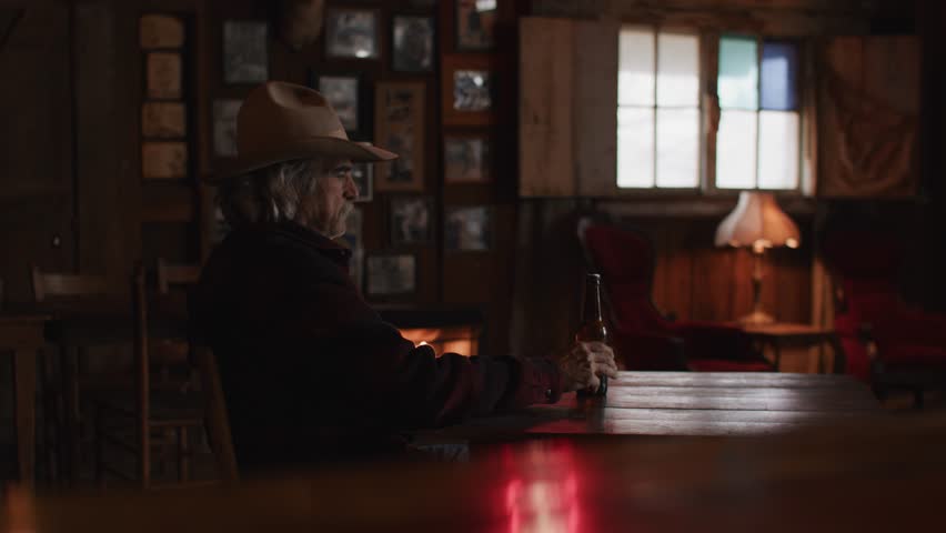 Man With Mustache Wearing Red Flannel and Cowboy Hat Sitting in Front of Fireplace in Old Rustic Saloon