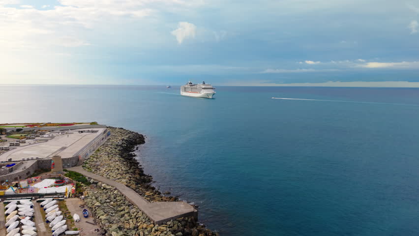 Drone advances from Genoa jetty toward cruise ferry as small motorboat approaches nearby.