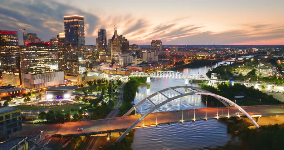 Driving cars on bridge highway near high-rise buildings in downtown district of Nashville, Tennessee, USA. American city with business financial district at sunset.