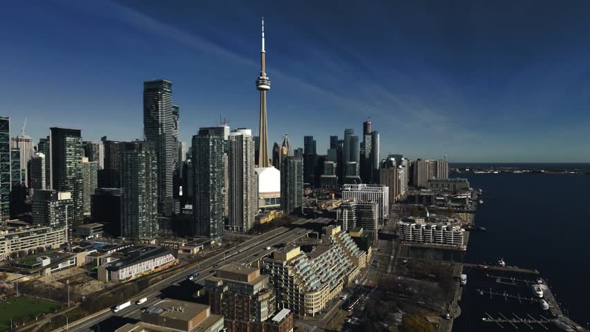 Drone Aerial of Toronto Coastal Waterfront Skyline at Midday featuring the CN Tower, Rogers Centre, Harbourfront, and the shoreline of Lake Ontario.