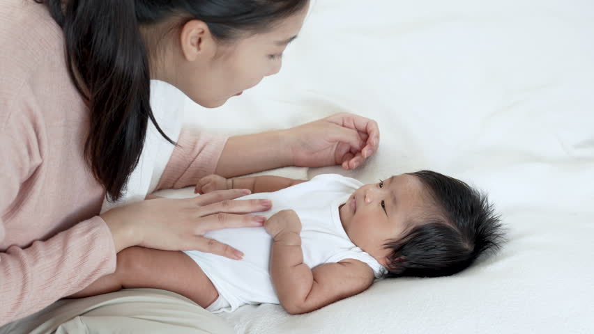 Young Asian mother play with her little newborn baby while baby yawning and ready to sleep.