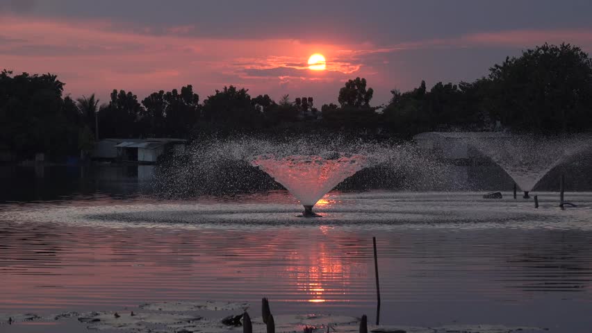 A sunset over a tranquil lake, with the sunlight shining through a water fountain.