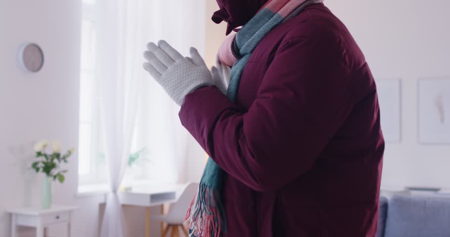 Close up cropped view of man in warm winter clothes and woolen gloves freezing, shaking from cold at home. Freezing person trying to warm up, calling emergency services. Heating problems concept.