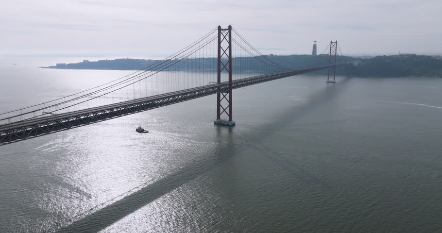 Cinematic aerial drone view of the red 25th April suspension bridge over the Tagus river in Lisbon, Portugal, with a single car crossing before a running event
