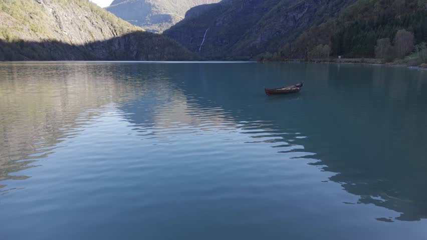 A lonely boat in turquoise green water of mountain lake in Norway. Drone footage