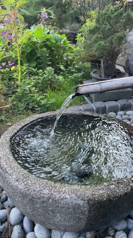 Traditional Korean bamboo water fountain flowing into a stone basin with green garden plants – calming natural ambiance
