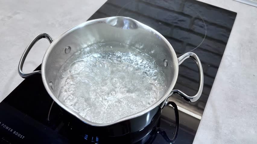 A stainless steel pot of boiling water on an induction hob, ready to cook pasta in a modern kitchen.